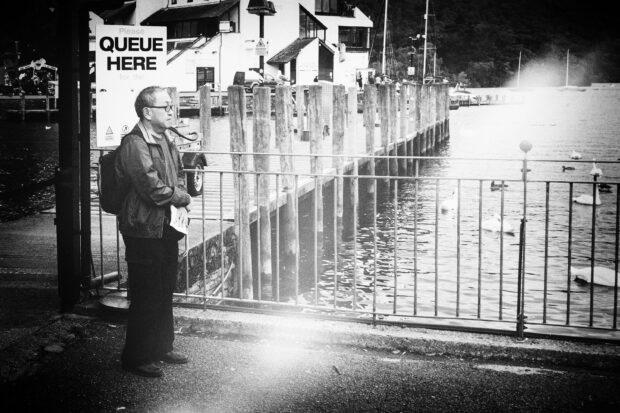 Man standing next to a 'Please queue here' sign.