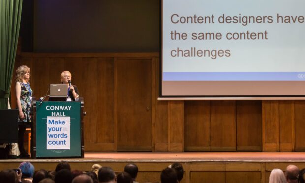 Presenters on stage at ConCon 5 with slide saying "Content designers have the same content challenges"