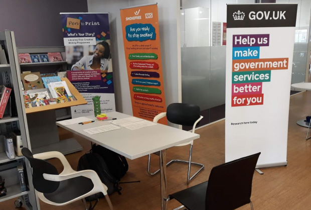 A table and chairs in a library with a big GOV.UK banner next to them