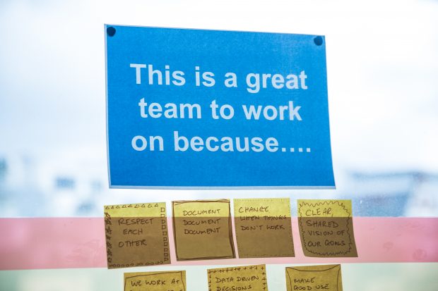 A poster that says ‘This is a great team to work on because…’. Underneath the poster there are several post-it notes, each in a different person’s handwriting. They say: ‘Respect each other’, ‘Document, document, document’, ‘Change when things don’t work’, ‘Clear, shared vision of our goals’.