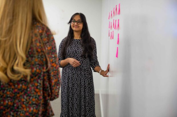 Suganya Sivaskantharajah standing next to a wall with post-its on looking at another woman. 