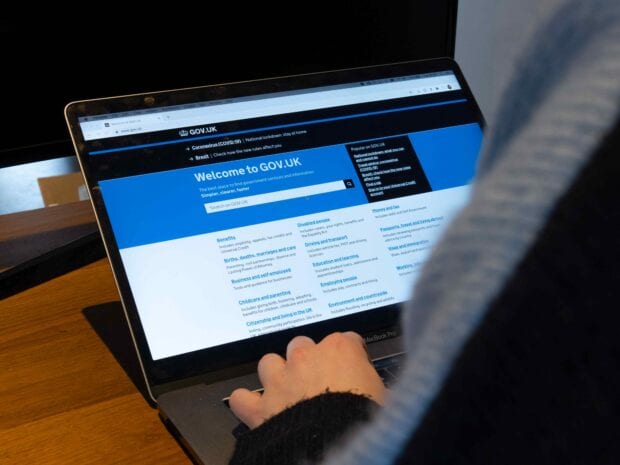 A person using a laptop with the screen displaying the GOV.UK homepage.