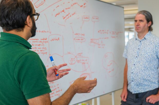 2 men standing by a whiteboard with an architecture diagram on