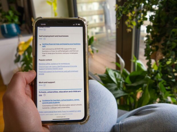 Person holding a smartphone visiting GOV.UK and interacting with the previous version of the accordion user interface element