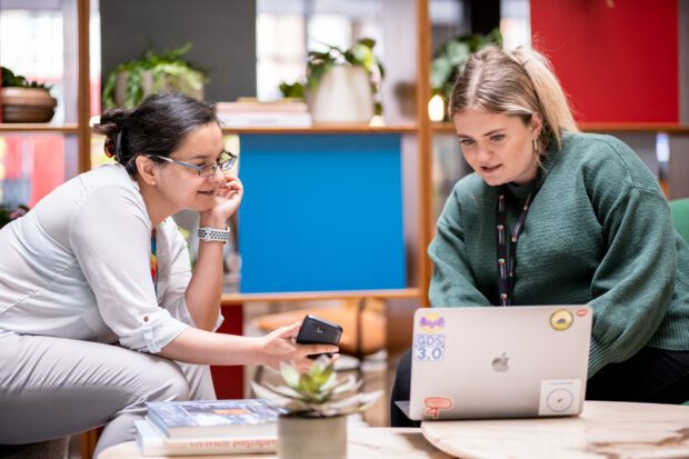 2 women looking at a laptop and mobile phone