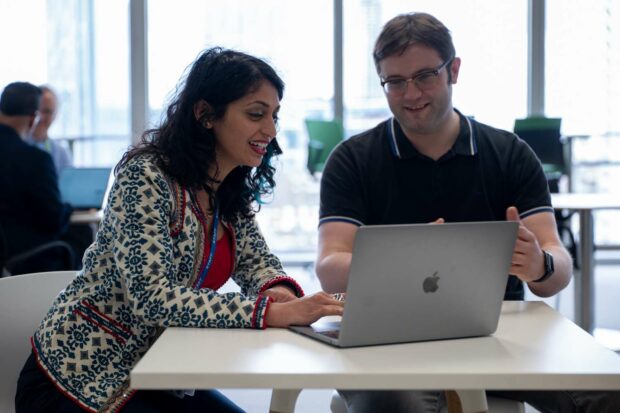 Two people sitting at a desk looking at a laptop. 