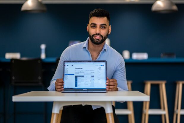 Man sitting at a table in an office with a laptop open. On the laptop screen there is the campaign template backend showing a page with title “Setting up GA4”.