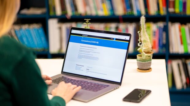 A woman sitting at a table with a laptop. On the laptop screen is the GOV.UK coronavirus page.