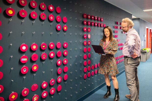 Two people standing by a wall that has a "G" made out of discs hanging on the wall