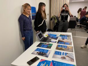 Students presenting their work on the table. They have printed posters demonstrating a speculative government scheme